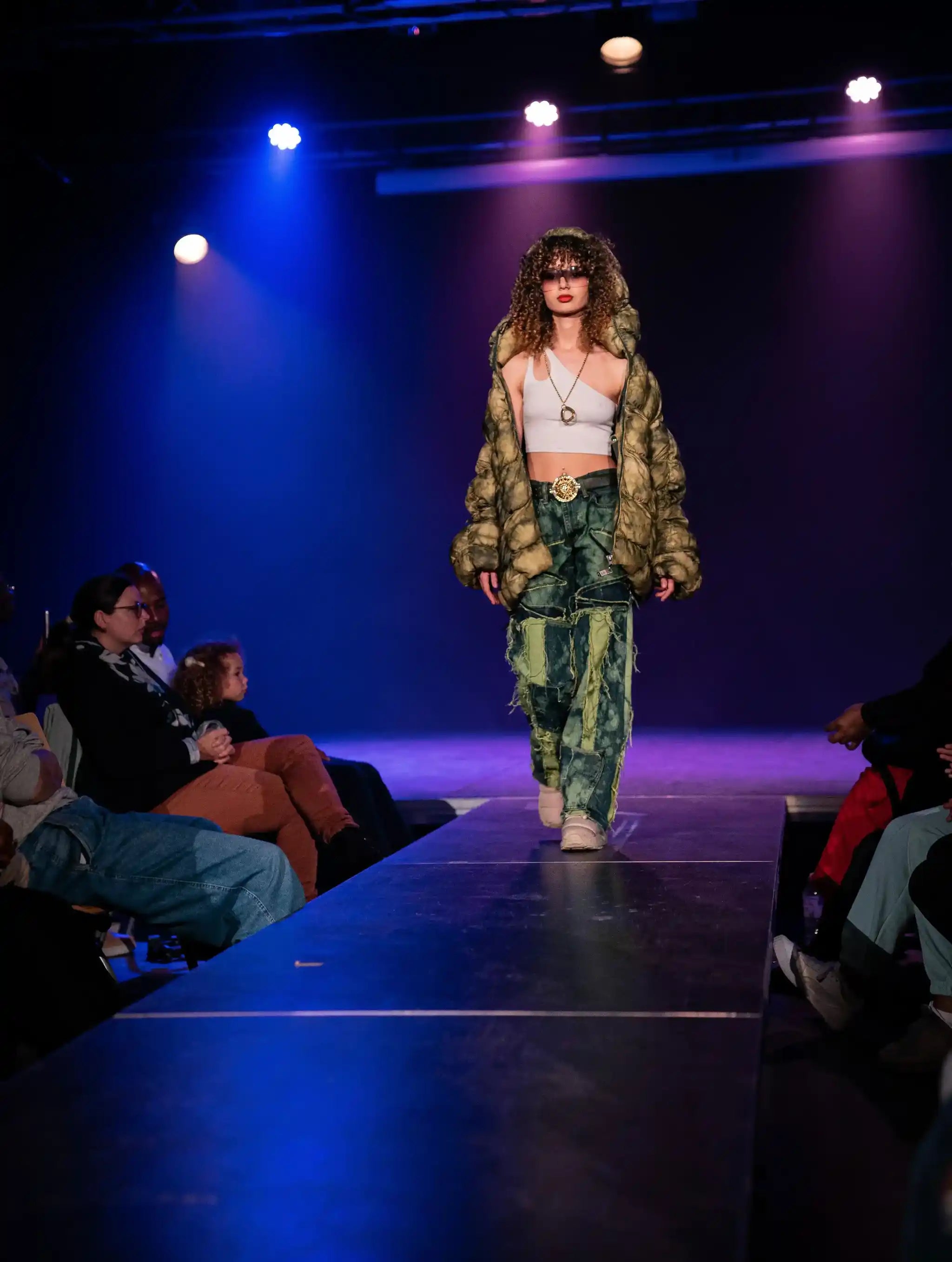 Runway photo: PrototypesParis green distressed patchwork denim with raw-edge panels and matching puffer jacket—handcrafted upcycled jeans, front view.